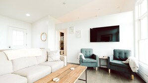 A modern living room with a sofa, a coffee table, two armchairs, a small side table, and a flat-screen TV mounted on the wall. - King Bed, Zero Entry, Close to Town (Sault Ste. Marie)