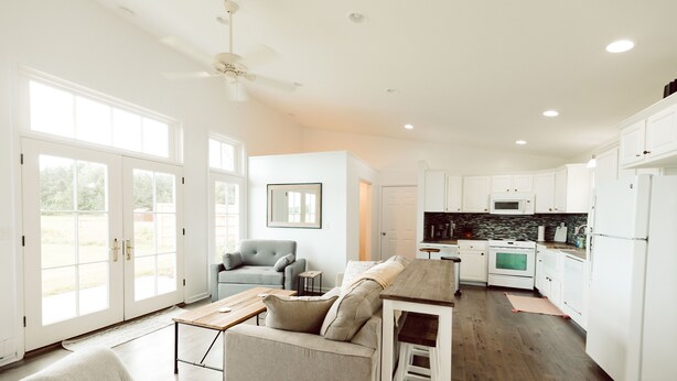 A spacious living area with a sofa, coffee table, and a kitchen with white cabinets and appliances. - King Bed, Zero Entry, Close to Town (Sault Ste. Marie)