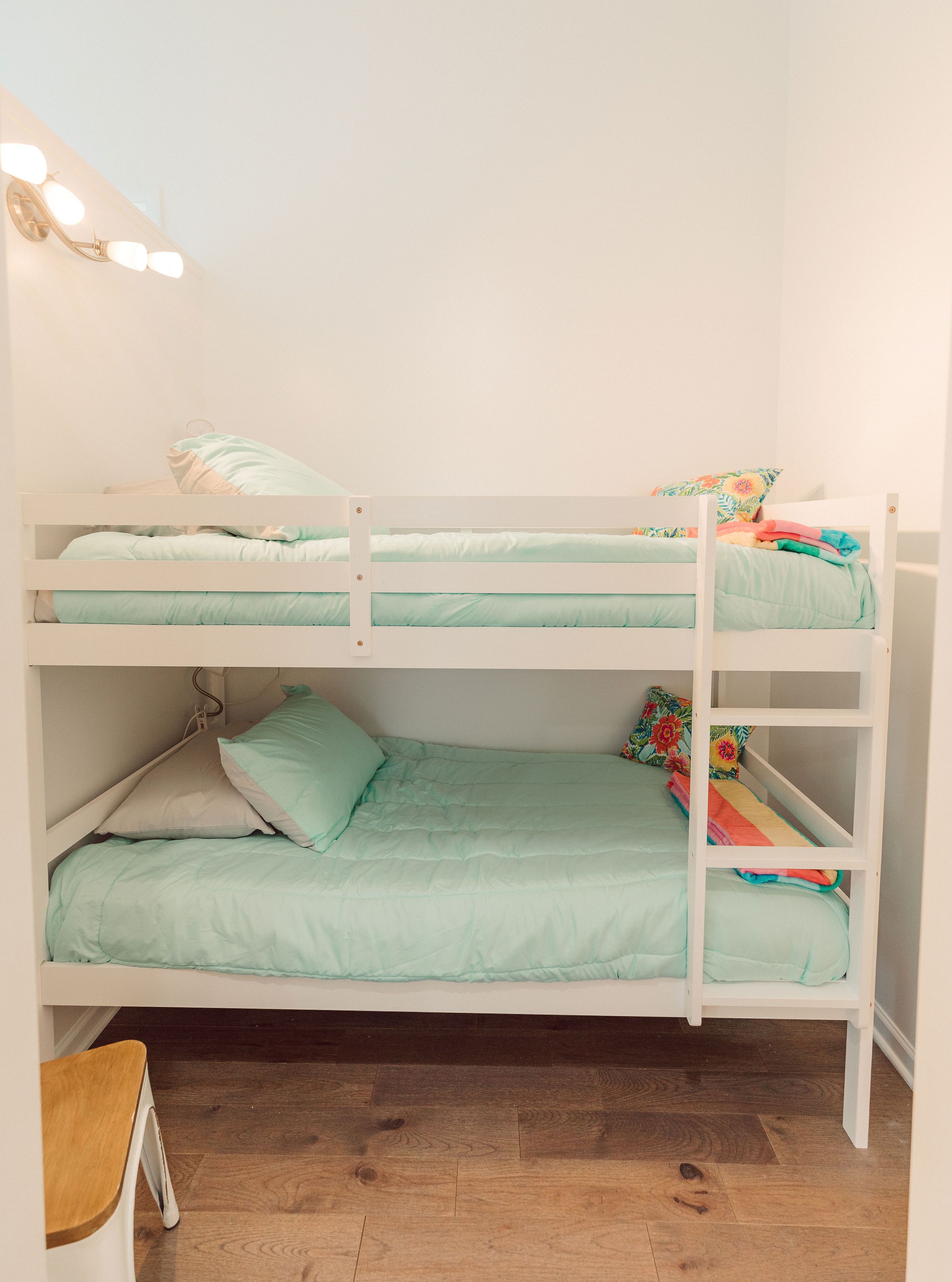 A bunk bed with two levels, each with a light green mattress and pillows.