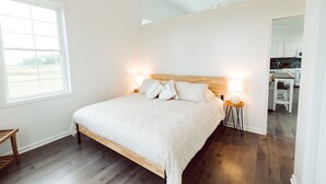 A bedroom with a large bed, a window, and a view of the kitchen. - King Bed, Zero Entry, Close to Town (Sault Ste. Marie)