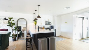 Una cucina moderna con mobili bianchi, un'isola centrale, contenitori per rifiuti in acciaio inossidabile e illuminazione a sospensione.