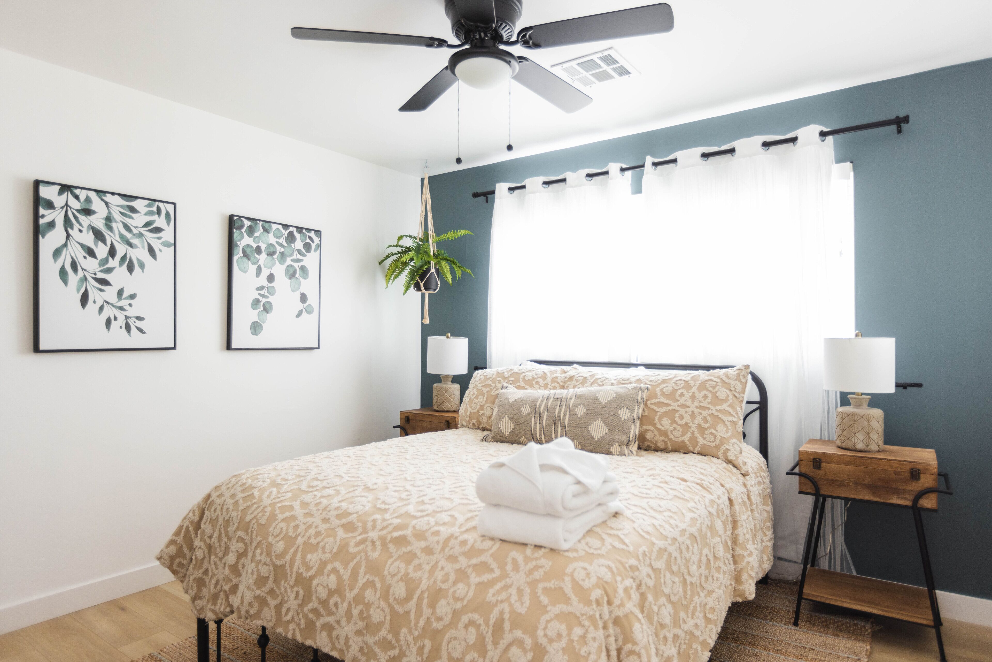 A bedroom with a bed, two bedside tables, a ceiling fan, and a window with curtains.