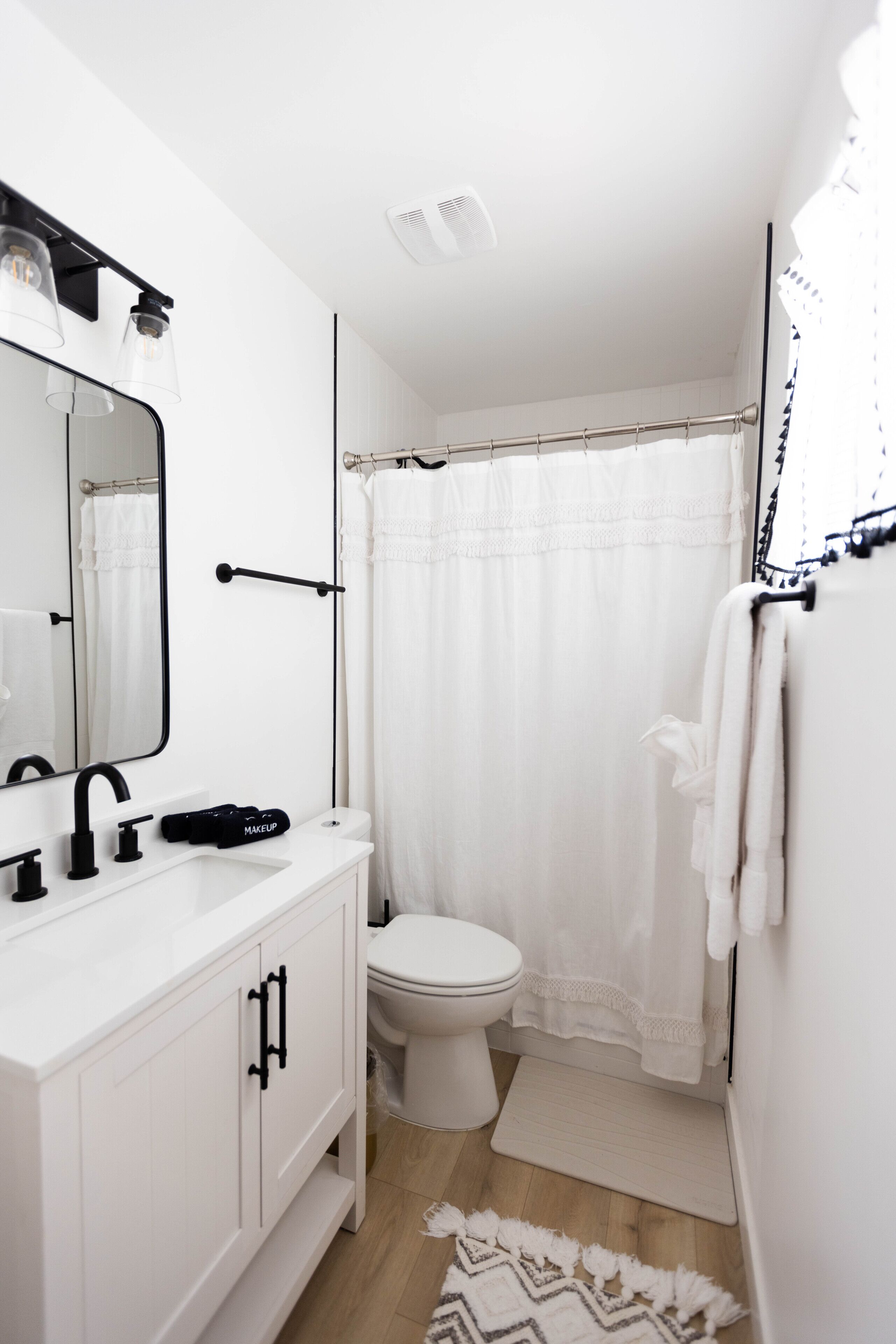 A modern bathroom with a white vanity, a large mirror, a toilet, and a shower curtain.