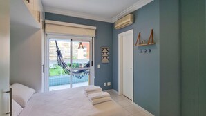 Un dormitorio con cama, ventana con vistas a edificios, puerta y aire acondicionado de pared.