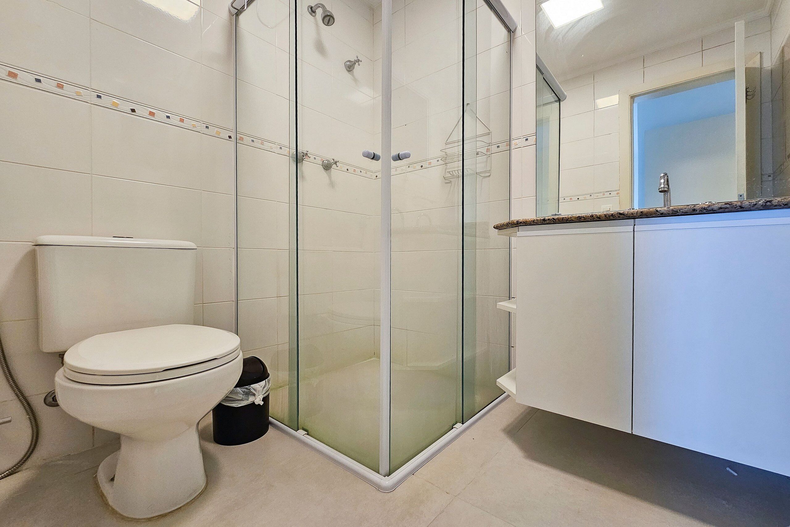 A bathroom with a glass-enclosed shower, a toilet, and a sink with a mirror above it.