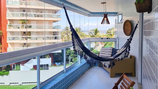 Un balcón con una hamaca, sillas de madera y vista a un edificio de varios pisos.