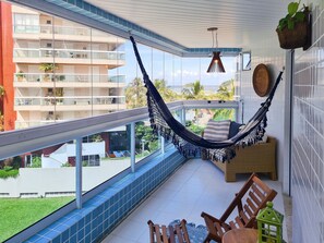 Un balcón con una hamaca, sillas de madera y vista a un edificio de varios pisos.