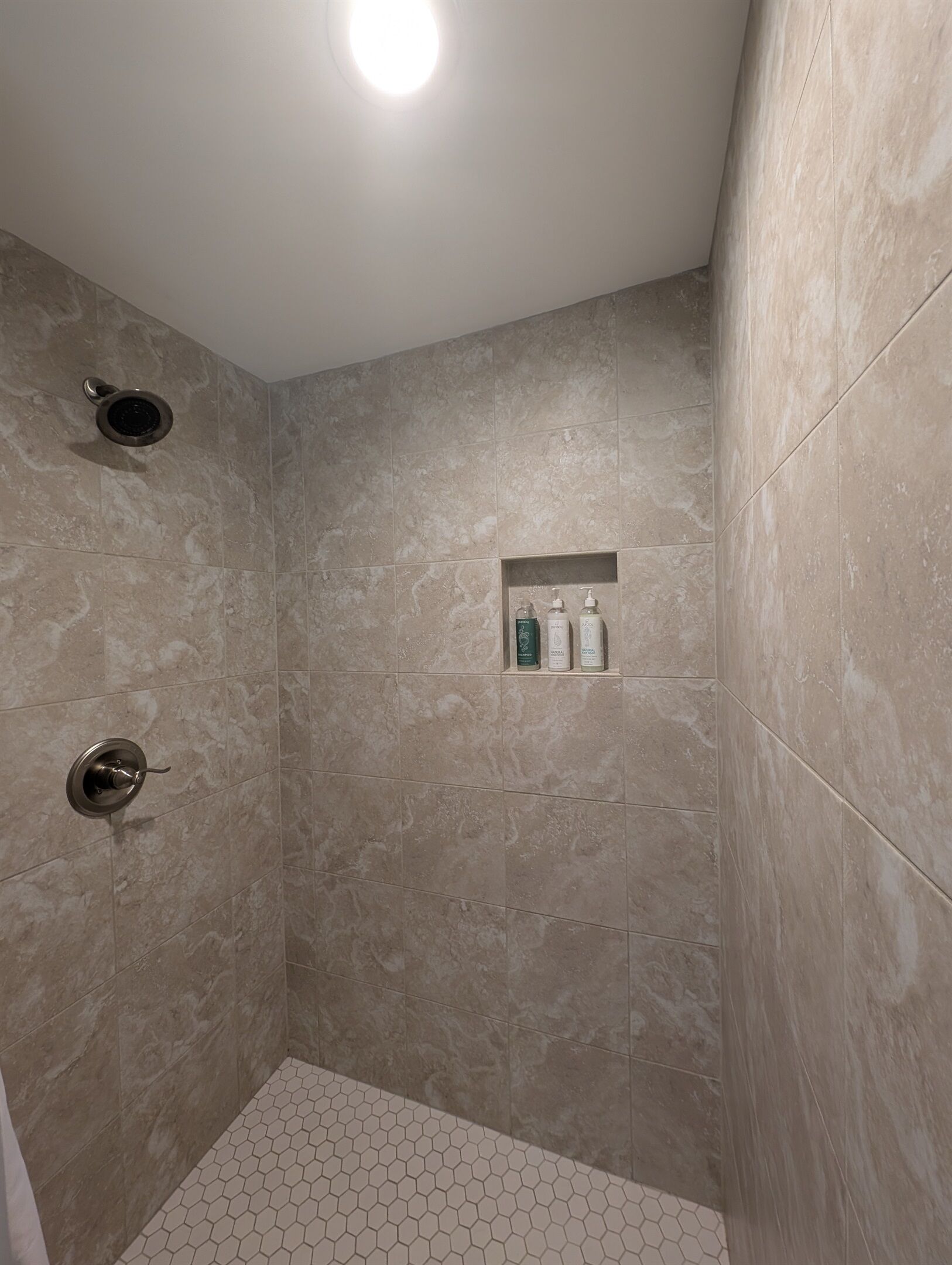 Un espace douche avec des carreaux de couleur beige, une étagère intégrée pour les articles de toilette et un motif hexagonal sur le sol.