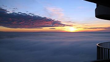 Vista al atardecer desde un balcón con barandilla, nubes abajo y cielo despejado.