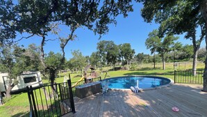 Una terraza de madera con piscina, rodeada por una valla y árboles.