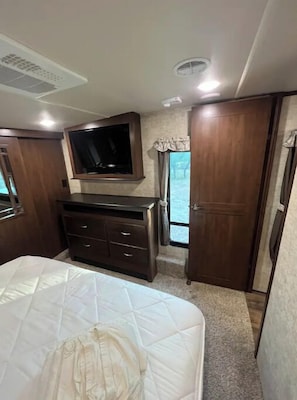 Ein Schlafzimmer mit Bett, Kommode, Fernseher und Fenster.