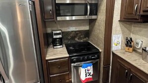 Una cocina compacta con un refrigerador de acero inoxidable, un microondas, una estufa y una cafetera.