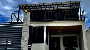 A modern two-story house with a covered entrance, stone facade, and a balcony with metal railings. - Moni's House, Terraza con Espectacular Vista al Mar, (Monteverde)
