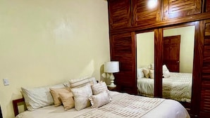 A bedroom with a large bed, wooden wardrobe, and a mirror. - Moni's House, Terraza con Espectacular Vista al Mar, (Monteverde)