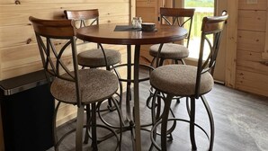 Un interior de madera con una mesa redonda y cuatro sillas, un cesto de basura pequeño y una ventana con vistas.