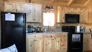 Cocina de cabaña de madera con refrigerador, estufa, microondas y gabinetes de madera.