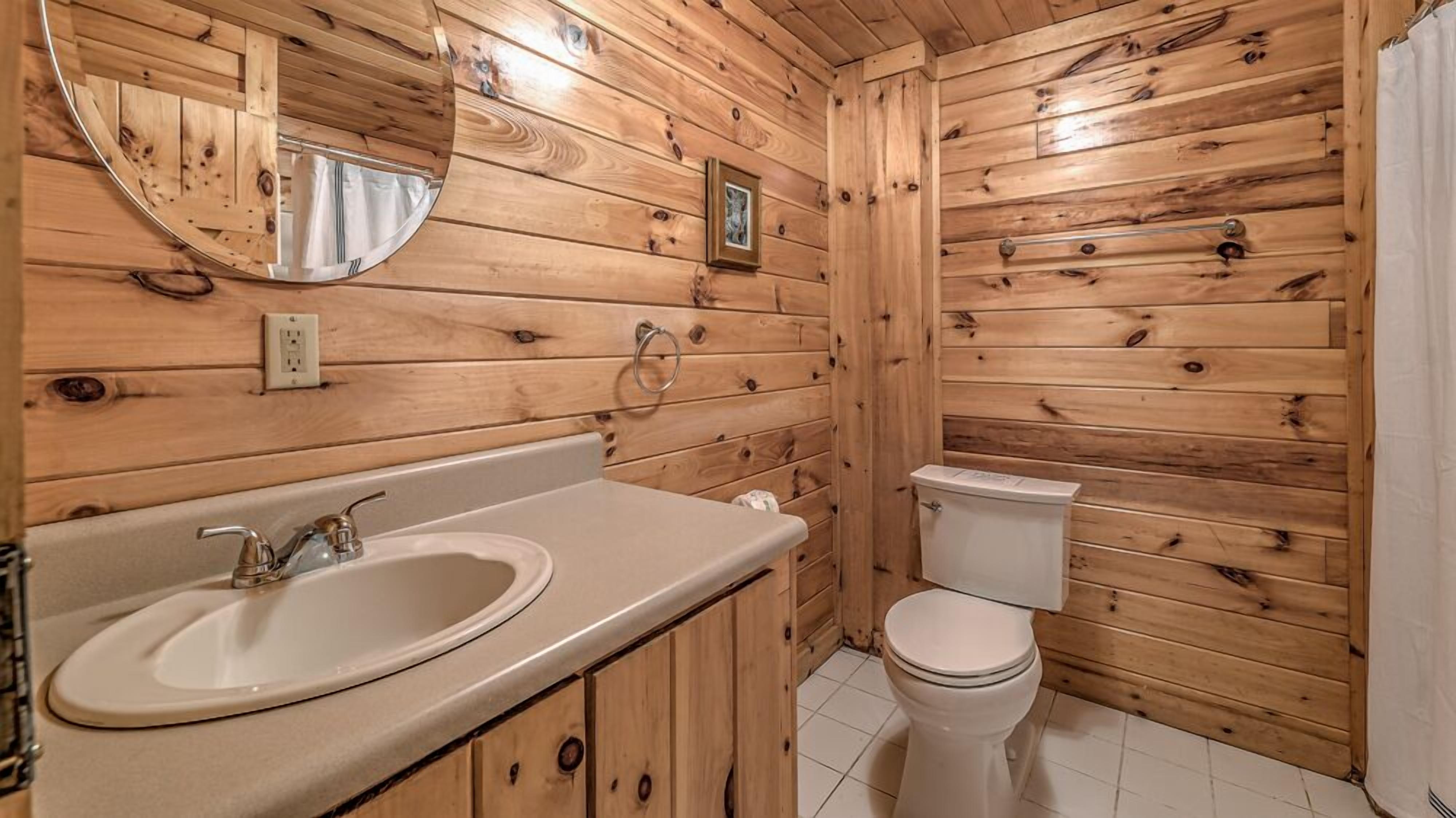 Bagno di una baita in legno con lavandino, specchio, WC e una luce ad anello a parete.