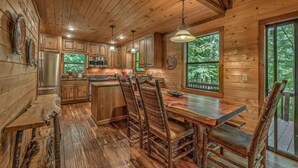 A wooden cabin kitchen with a central island, wooden cabinets, and a large window overlooking greenery. - Away to the Lake - Lake Blue Ridge dock | Hot Tub Pool Table | Ping Pong | Fire pit (Blue Ridge)