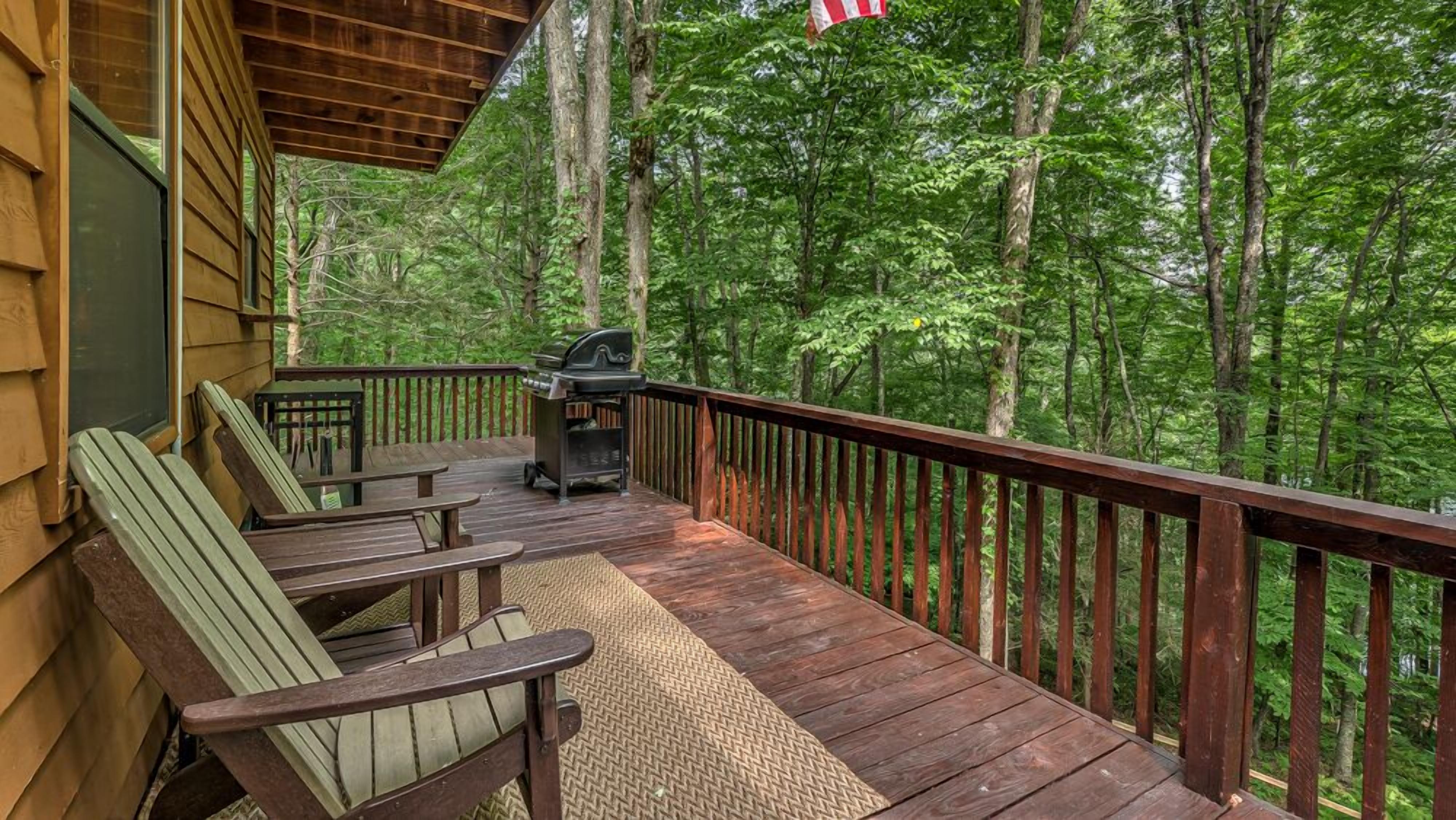 Eine Holzterrasse mit Sitzgelegenheit und Grill, umgeben von dichtem Wald.