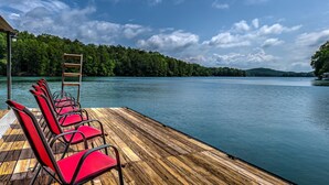 A wooden deck with red chairs and a ladder, overlooking a calm lake with a forested shoreline. - Away to the Lake - Lake Blue Ridge dock | Hot Tub Pool Table | Ping Pong | Fire pit (Blue Ridge)