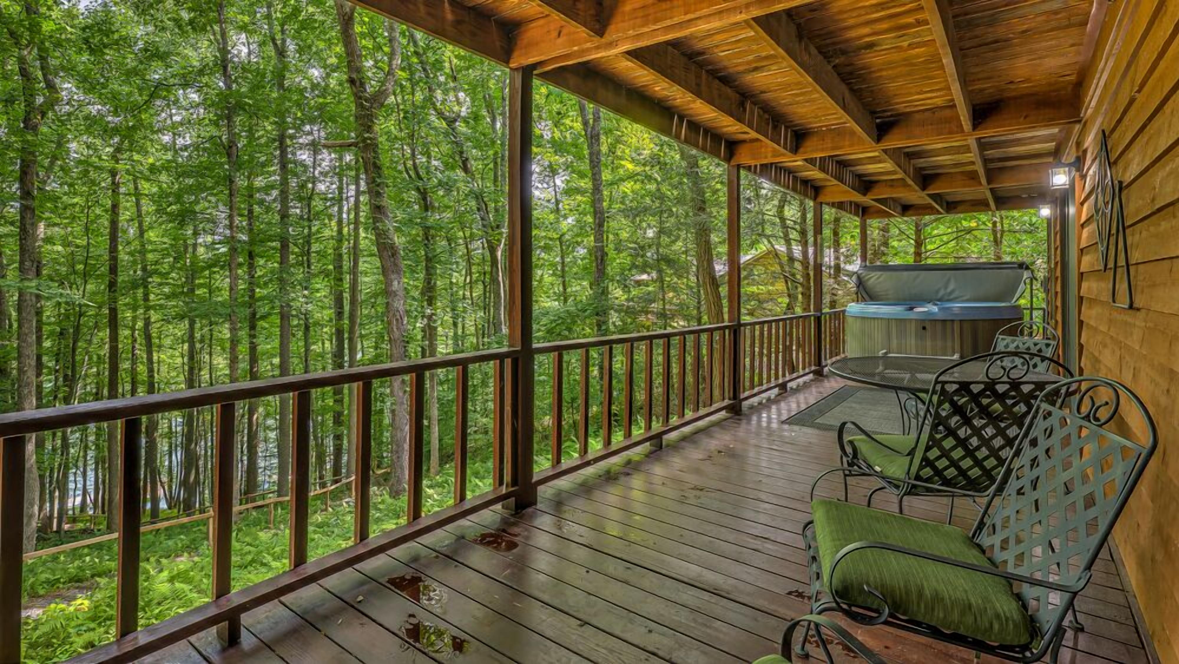 Une terrasse extérieure couverte avec des rampes en bois, un jacuzzi et des chaises en métal.