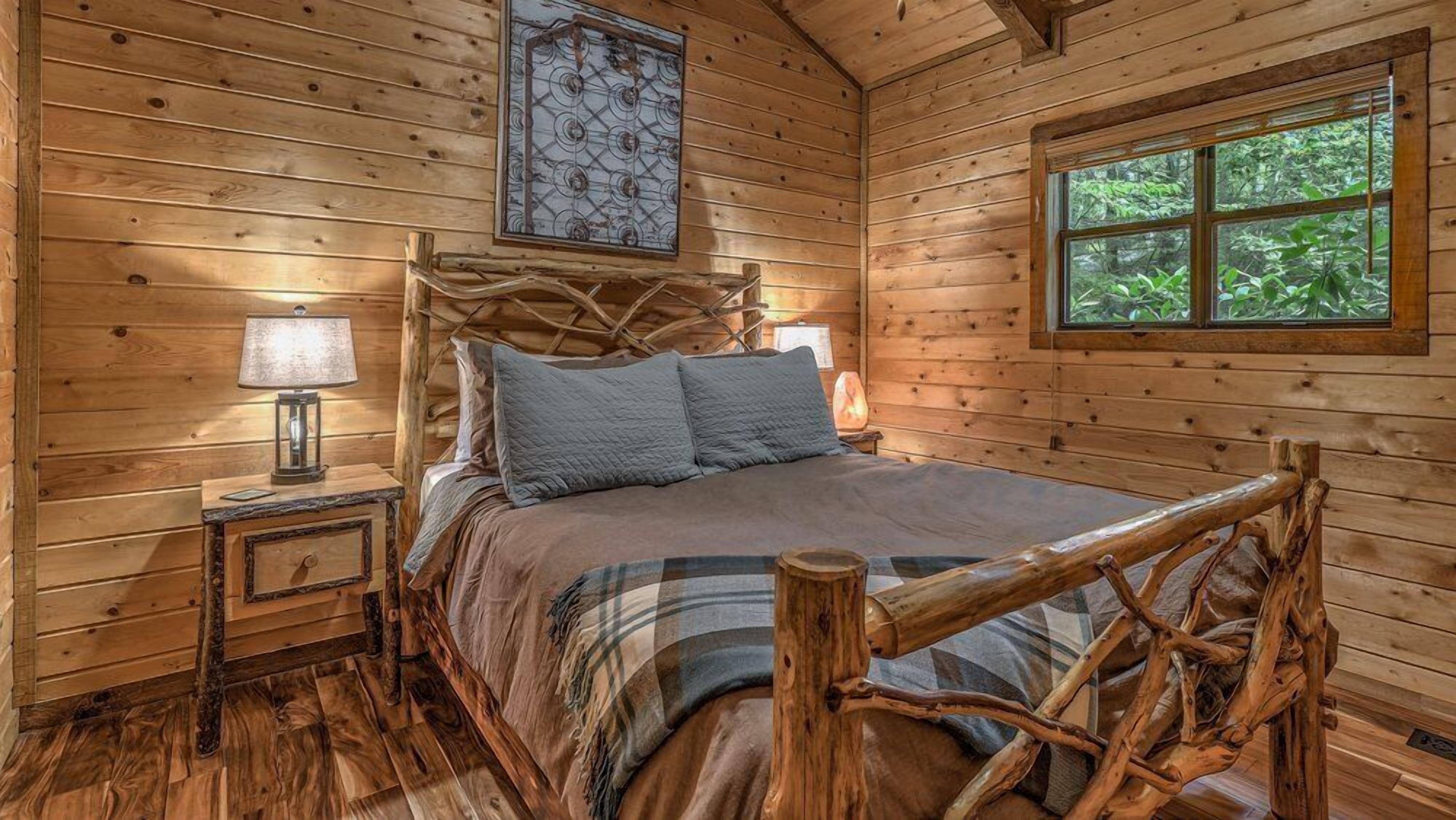 A wooden cabin bedroom with a bed, a nightstand, a window, and a decorative wall piece.