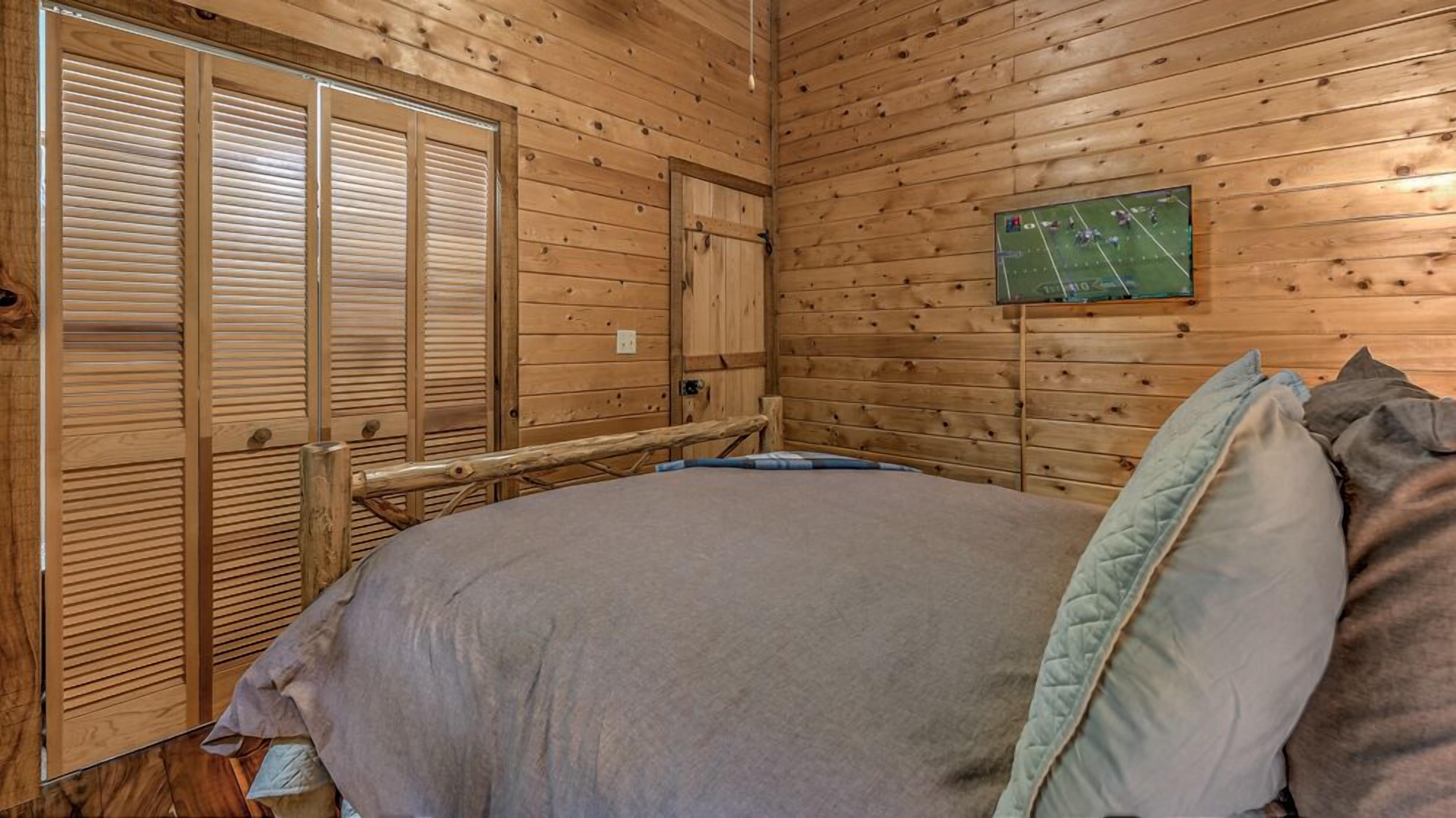 Une pièce en bois avec un lit, une porte en bois et un téléviseur fixé au mur.