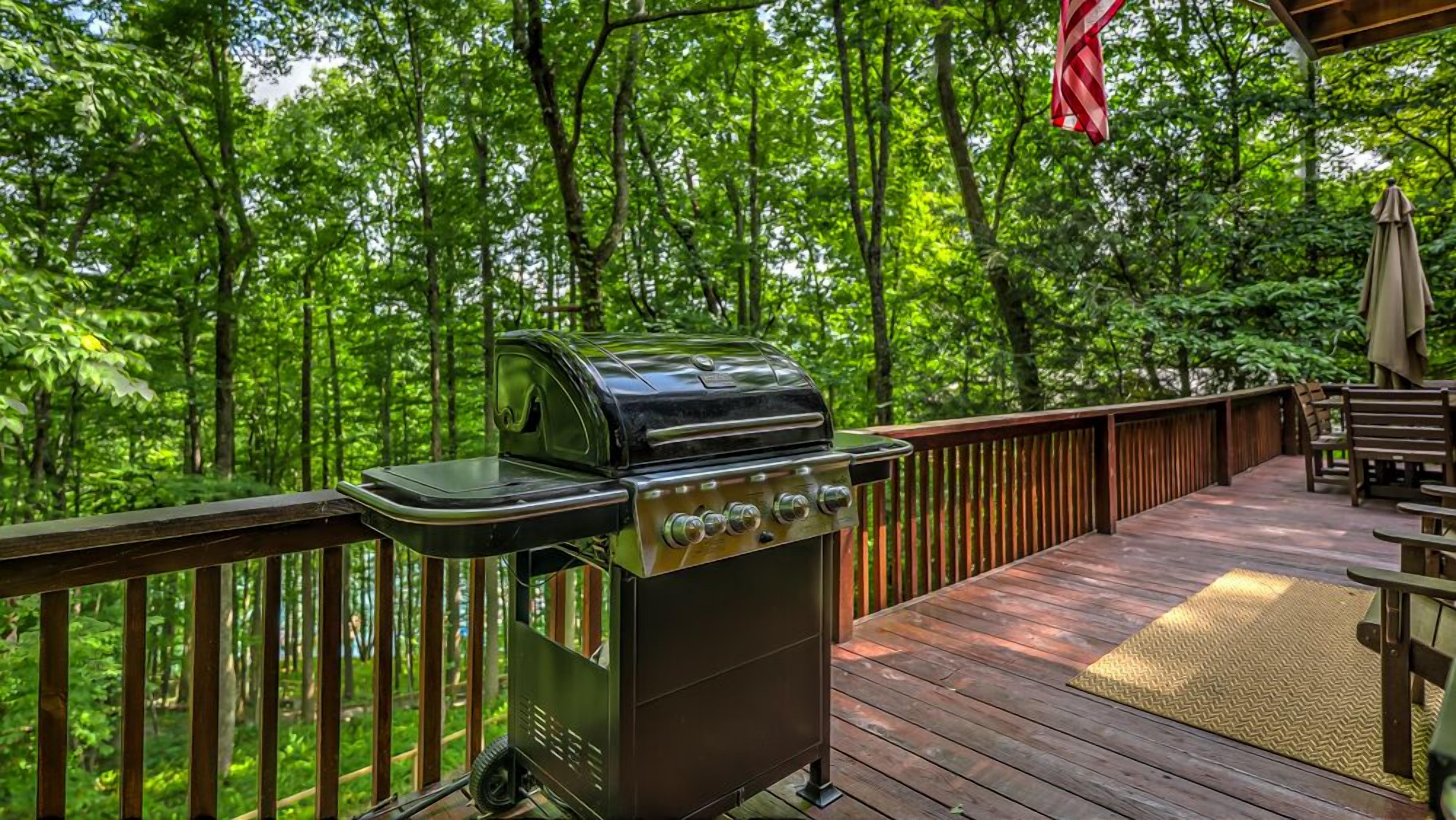 A deck with a portable grill, wooden railings, and outdoor furniture.