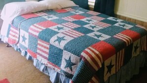 Une chambre à coucher avec un lit recouvert d’une courtepointe, deux fenêtres avec des rideaux et un tableau encadré au mur.