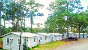 Une rangée de petites cabanes à un seul étage, avec une allée en gravier, entourées d’arbres.
