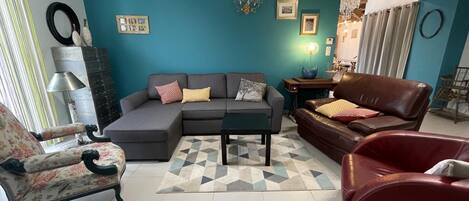 A living room with a teal wall, a sectional sofa, a brown leather couch, a patterned armchair, a coffee table, and a geometric rug.