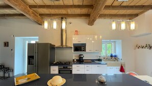 A modern kitchen with a central island, stainless steel appliances, and wooden ceiling beams. - Eiherabidia - Beyrie SUR Joyeuse (BEYRIE SUR JOYEUSE)
