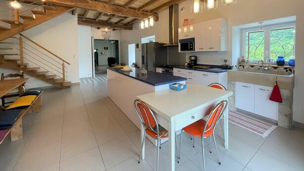 A modern kitchen with a central island, white cabinets, and a dining area with orange chairs. - Eiherabidia - Beyrie SUR Joyeuse (BEYRIE SUR JOYEUSE)