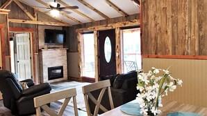 A rustic interior with exposed wooden beams, a fireplace, a television, and a dining area with a vase of flowers. - "Eagle's Nest" Tree House #5 w/ 2-person hot tub (Potosi)
