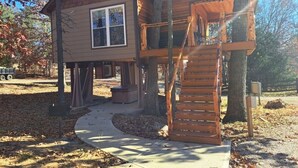 A wooden cabin with a covered porch and a staircase leading to an upper level. - "Eagle's Nest" Tree House #5 w/ 2-person hot tub (Potosi)