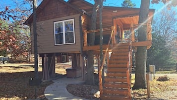 A wooden cabin with a covered porch and a staircase leading to an upper level.