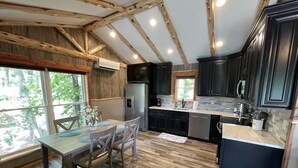 A kitchen with wooden beams, a dining table with chairs, a refrigerator, and a window with a view of trees. - "Eagle's Nest" Tree House #5 w/ 2-person hot tub (Potosi)