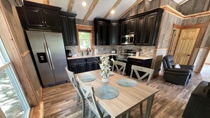 A modern kitchen with dark cabinets, stainless steel appliances, and a wooden dining table with placemats. - "Eagle's Nest" Tree House #5 w/ 2-person hot tub (Potosi)