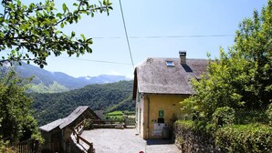 A rustic mountain house with a stone entrance, a small wooden structure, and a view of lush green hills in the background. - LE Cailhabas - Lescun (LESCUN)