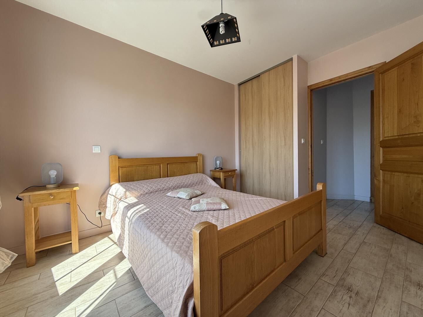 A bedroom with a wooden bed, bedside tables, a wardrobe, and a ceiling light fixture.