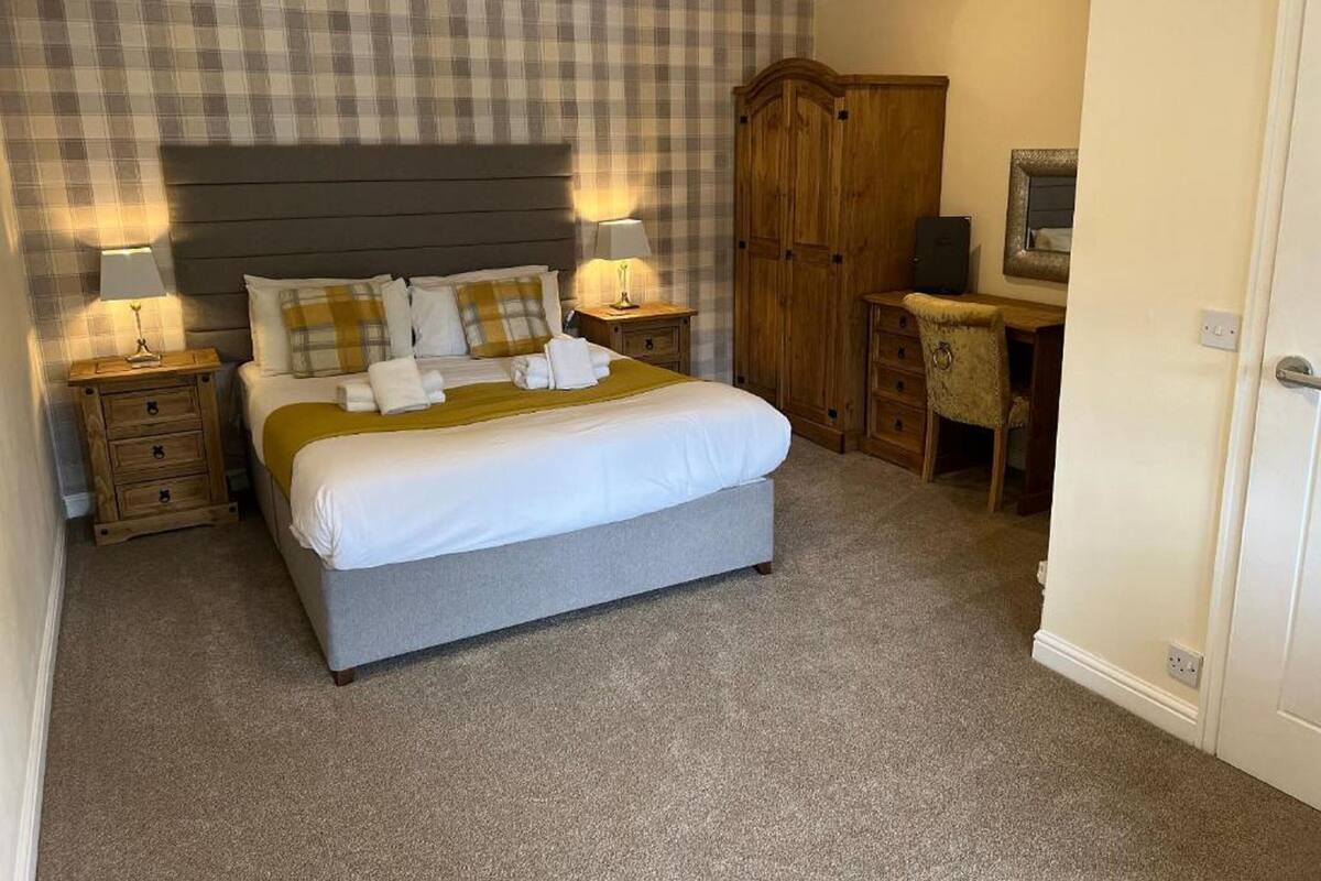 A neatly arranged bedroom with a bed, two bedside tables, a wardrobe, and a desk.