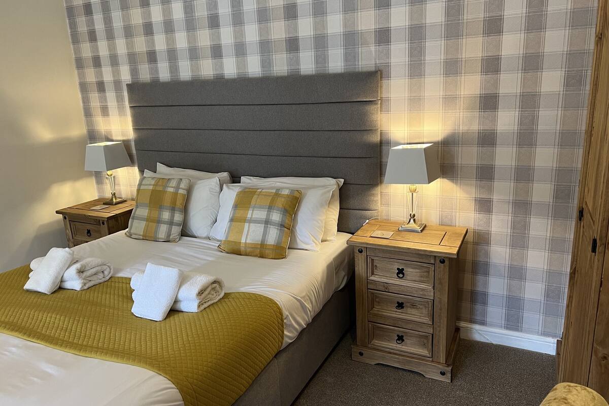 A neatly made bed with a headboard, two bedside tables with lamps, and a plaid-patterned wall.