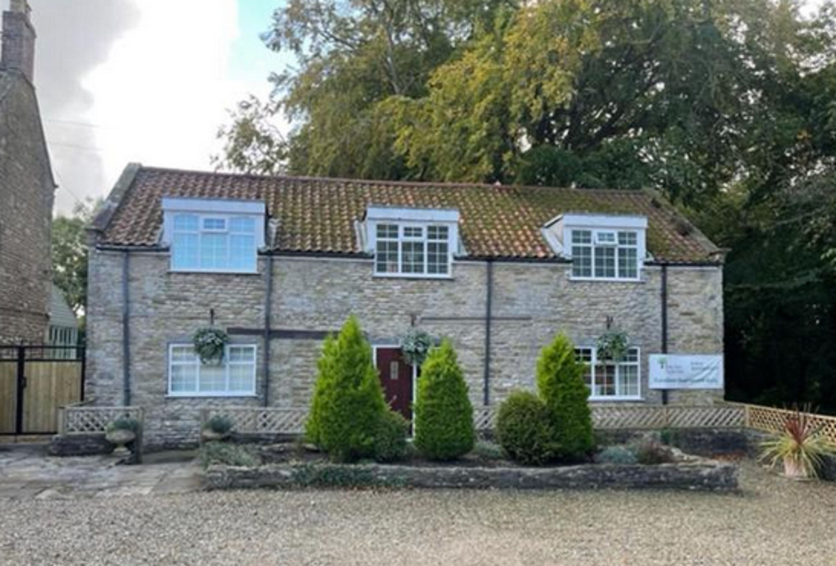 A stone building with a tiled roof, multiple windows, and a gravel driveway.
