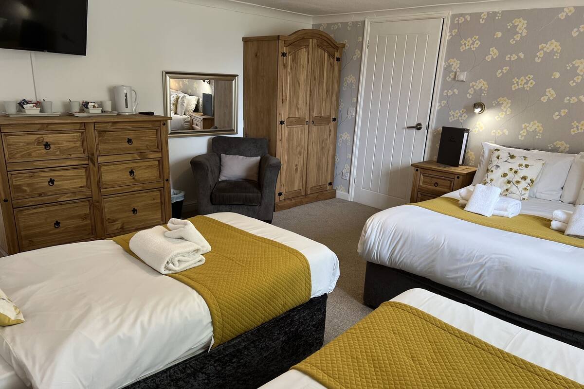 A hotel room with two beds, a wooden wardrobe, a chair, a television, and a mirror.