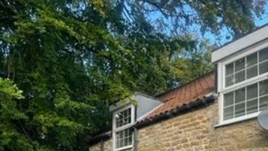 Un edificio de piedra con techo de tejas, una ventana con diseño de cuadrícula y un patio con mesa y sillas.