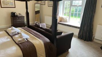 A four-poster bed with a canopy, a sofa, a dresser, and a window with a view of greenery.