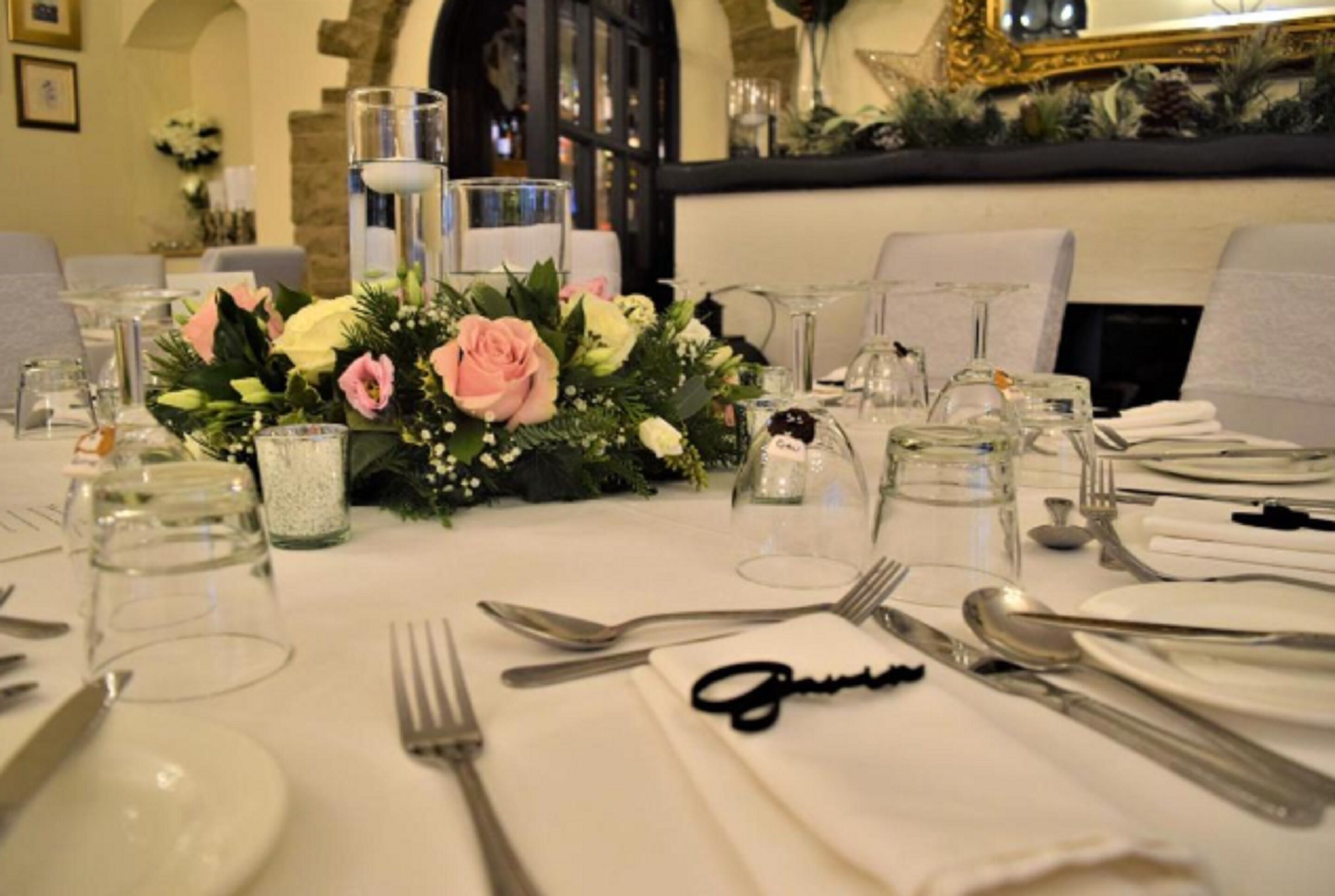 Une table dressée pour le repas, agrémentée d’un centre de table composé de fleurs et de bougies, entourée de chaises et de couverts.