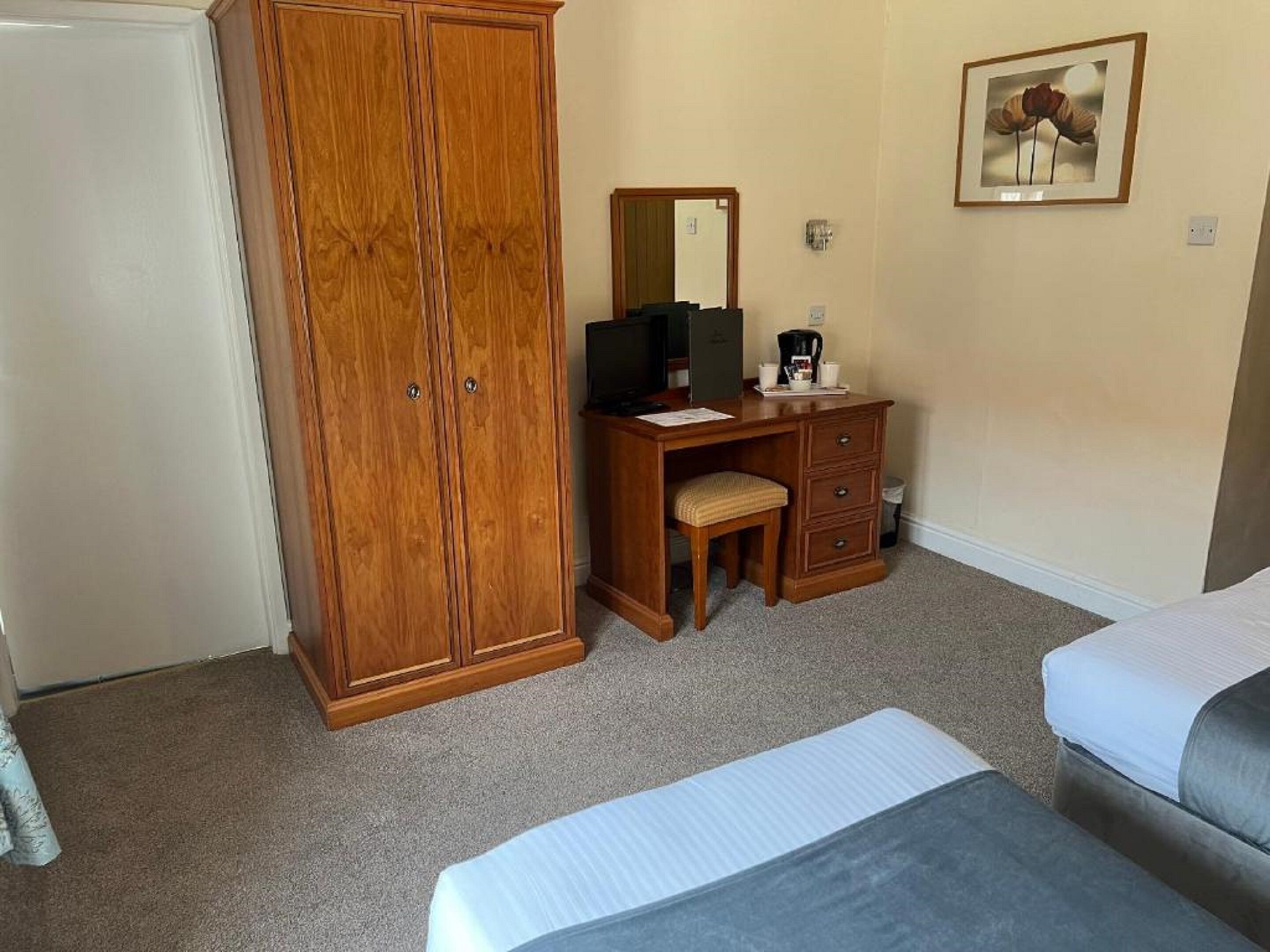 Un dormitorio con un armario de madera, un escritorio con silla, una cama y un cuadro enmarcado en la pared.