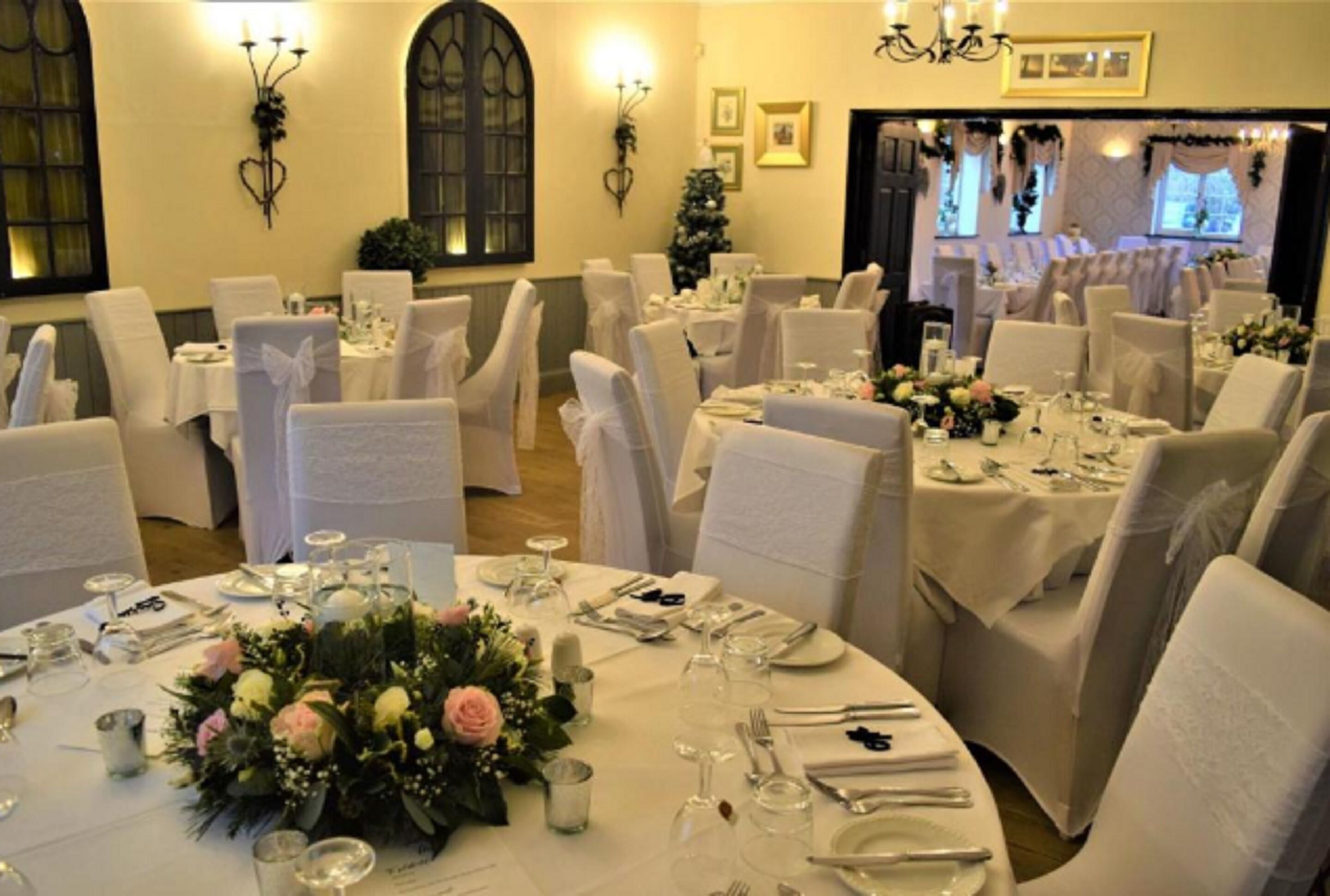 Un salón de banquetes con mesas redondas dispuestas para un evento formal, con manteles blancos, centros de mesa florales y cubertería ordenada.