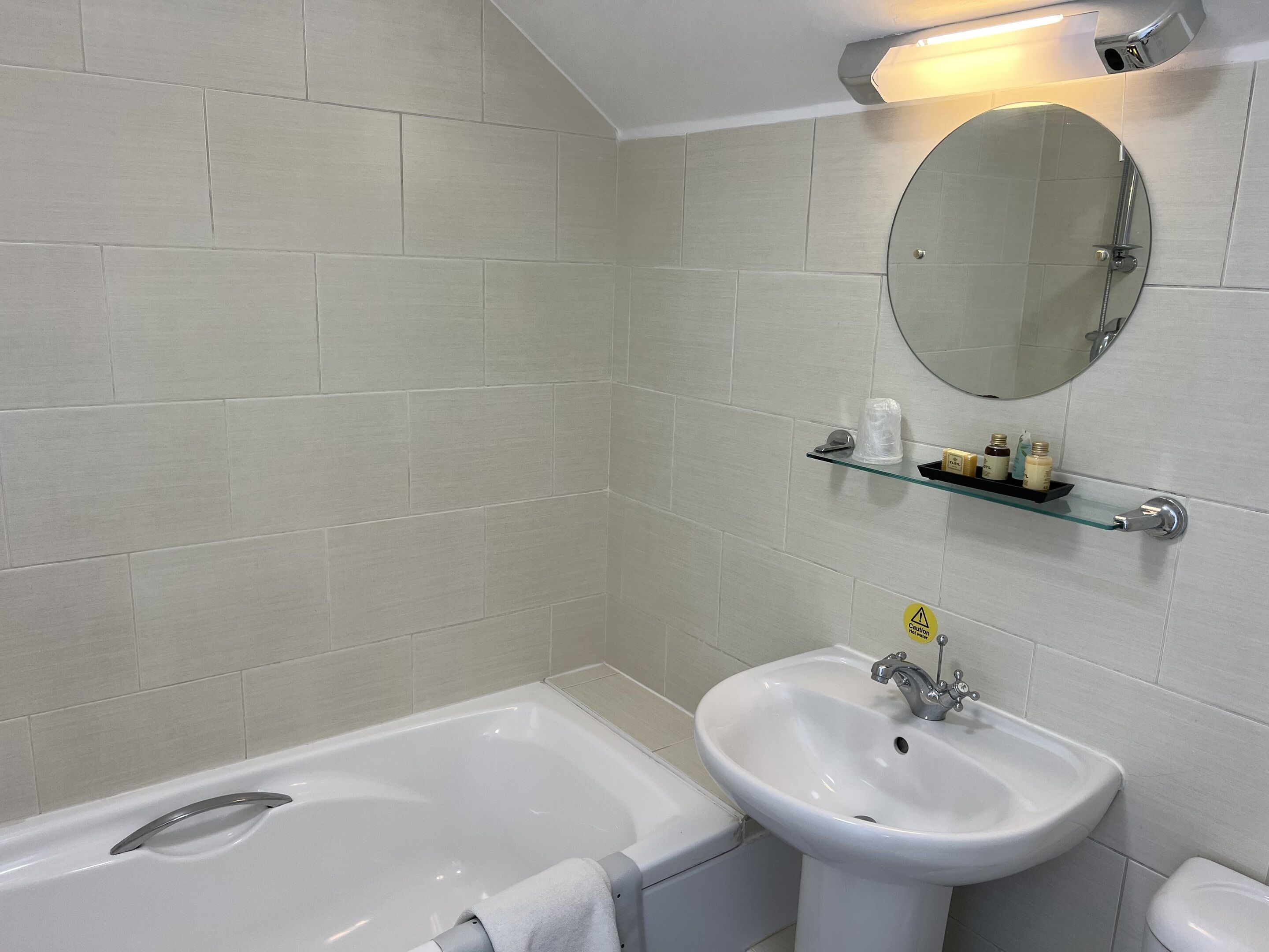 A bathroom with a bathtub, a sink, a mirror, and a shelf with toiletries.